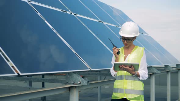 A Female Engineer Communicating on a Walkie-talkie Near a Solar Construction. Alternative Energy