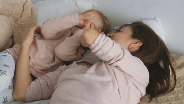 Mother Plays with Little Daughter on the Bed