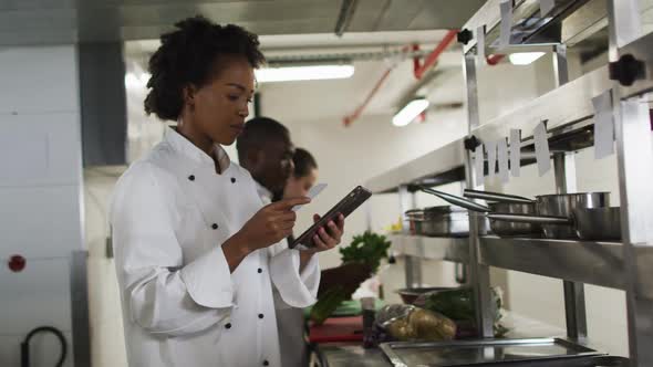 African american female chef taking orders and using tablet in restaurant kitchen