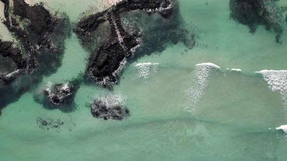 several waves come from the deep emerald ocean and they make beautiful bubbles. black rocks are uniq