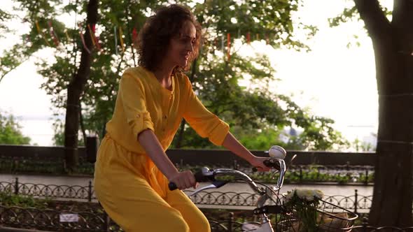 Attractive Woman in Long Yellow Dress is Cycling Through the City in Summertime on the Cycle with