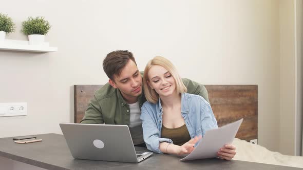 Young Happy Caucasian Spouses Sitting with Laptop and Documents