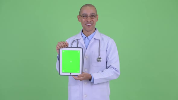 Happy Bald Multi Ethnic Man Doctor Showing Digital Tablet and Looking Surprised