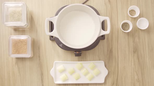 Female chef pouring milk in a cooking pot on an electric stove, top shot static