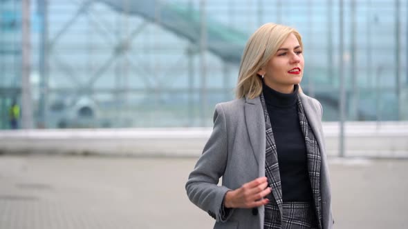 Blonde Girl Rolls a Suitcase Near the Airport Terminal