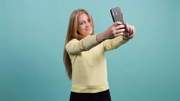 Funny Young Blonde Haired Woman Making Selfie on Turquoise Background.