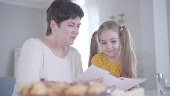 Adult Brunette Caucasian Woman and Little Girl Discussing Recipe of Pancakes for Shrove Tuesday