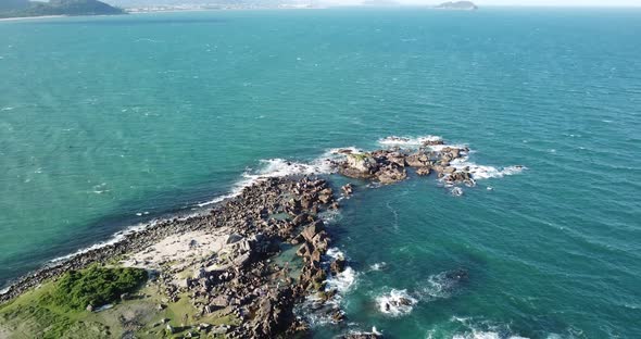 Aerial footage of the the beautifu rocks and sunny beach of Armação in Florianópolis, Brazil.