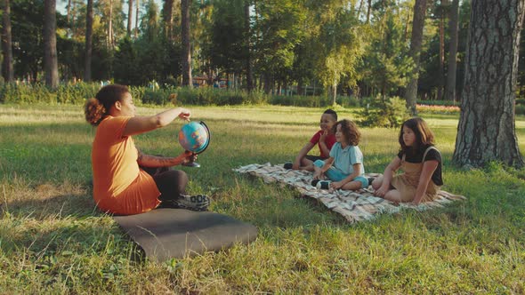 School Teacher Pointing on Globe Asking Questions to Pupils Outdoors