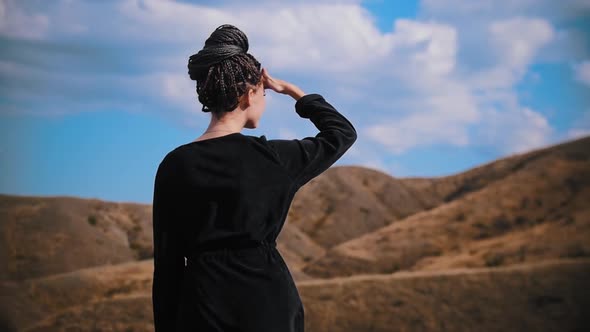 Young Woman with Dreadlocks Standing on the Pick of a Mountain and Looking Around