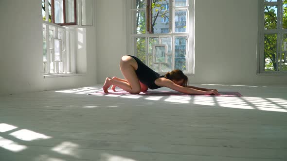 Adorable Young Red-haired Healthy Caucasian Woman Practicing Yoga on the Mat in the White Large Room