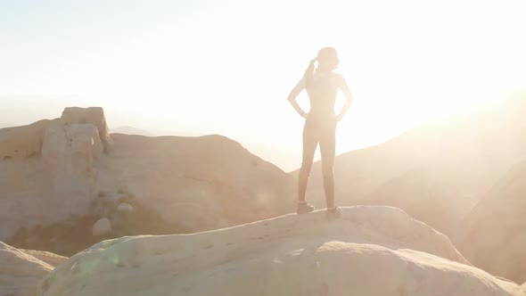 Woman hiker stands on mountain top in sunlight