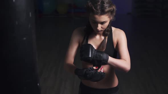 Woman Taking on Boxing Gloves on Hands with Black Boxing Wraps in Dark Room