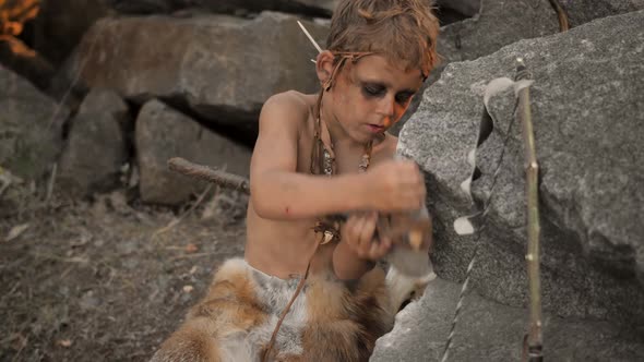 Caveman Manly Boy Making Primitive Stone Weapon in Camp