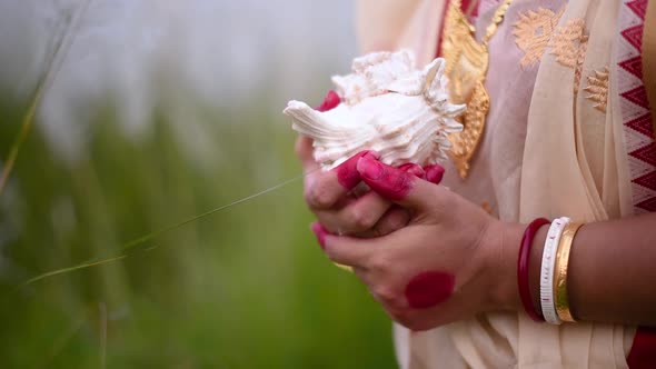 The hands of a newly wed Indian woman wearing saree holding a shankha or conch shell in a field outd