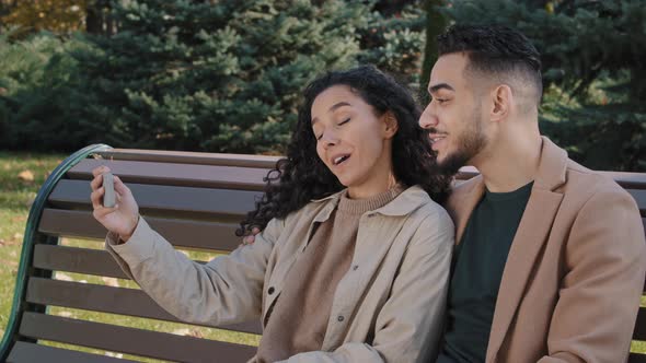 Hispanic Couple Making Video Call Using Smartphone in Autumn Park Guy and Girl Waving Hello Young