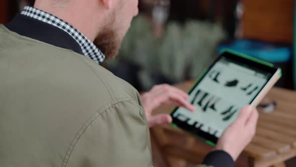 Bearded Man Is Choosing Shoes in Online Store By Tablet Browsing Site