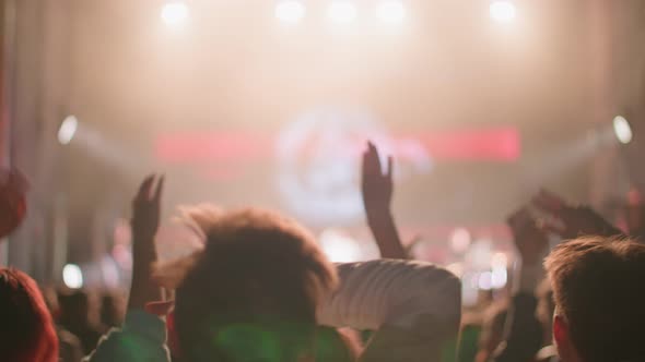 Rock Band Performing at Concert in a Night Silhouettes of Fans Raise Hands in Front of Bright