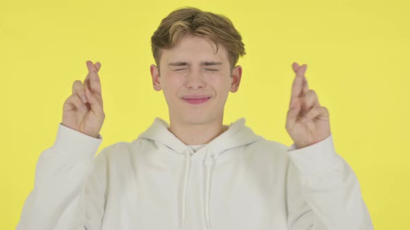Young Man Praying with Fingers Crossed on Yellow Background