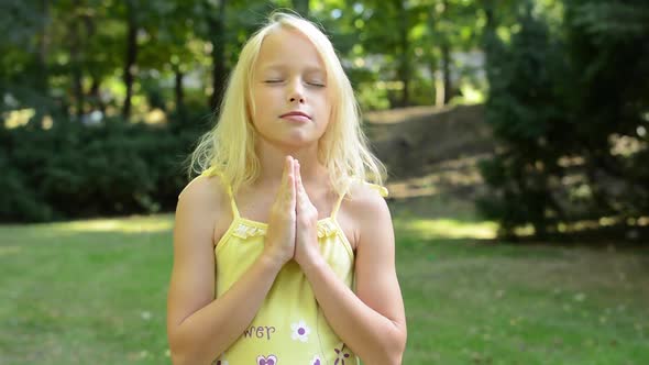 Little Cute Girl Prays in the Park with Prayer Hands Together