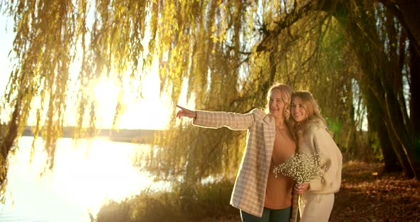 Pregnant Mother with Blonde Adult Daughter in Beige Clothes in Autumn Evening Park