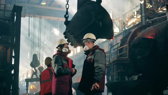 Steel Workers in Protection Wear are Talking in the Factory