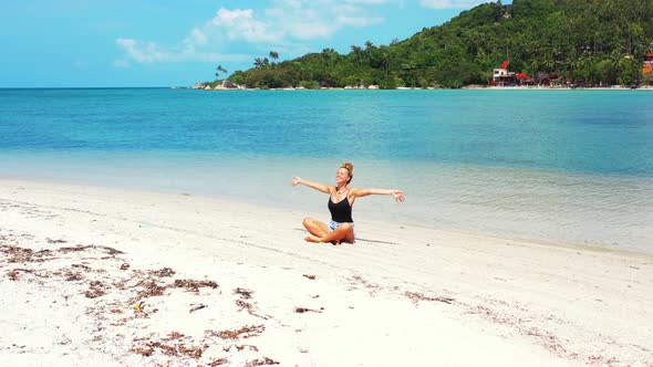 Happy woman with a big smile practicing yoga and meditating on the sandbar in Thailand. Leisure and