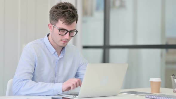 Thumbs Down By Young Man with Laptop in Office