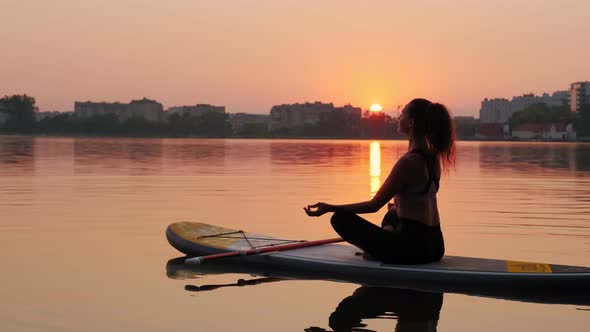 Young Woman Doing Yoga on SUP Board at Sunset