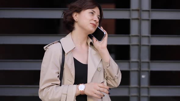 Cute Woman Chatting in Smartphone in Trench Coat