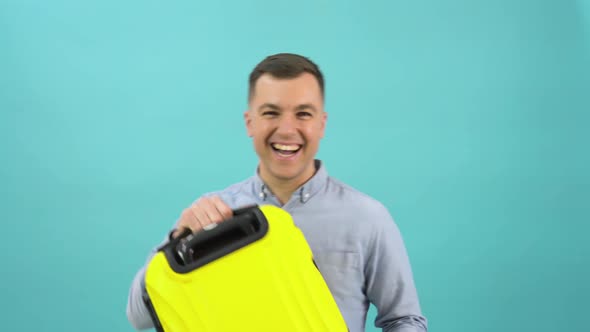 Happy Positive Man in a Blue Shirt Happily Shows Off a Stylish Yellow Plastic Suitcase in His Hands