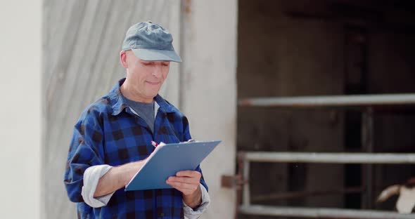 Farmer Analyzing and Writing on Clipboard Against Cowshed