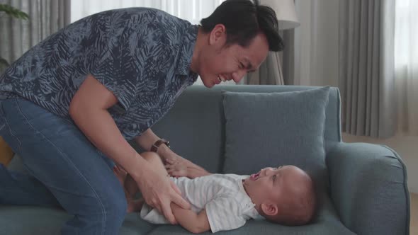 Asian Father And Son Playing On Sofa In Home