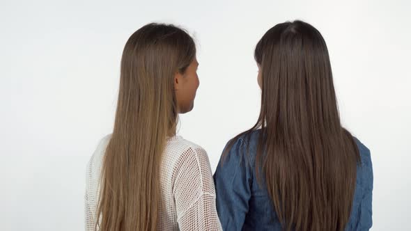 Rear View Shot of Two Female Friends Smiling To the Camera Over Their Shoulders