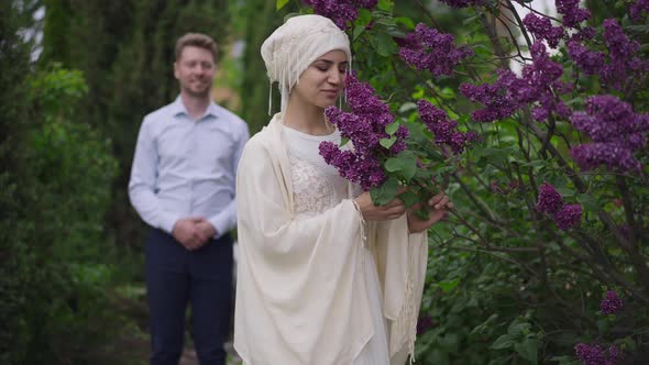 Charming Middle Eastern Bride Smelling Fragrance of Blooming Tree Branch As Smiling Happy Caucasian