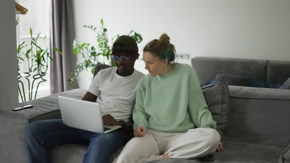 Biracial Couple Sitting on Sofa with Laptop Using Smartphone for Ecommerce