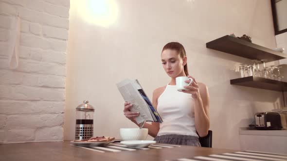 Woman With Newspaper Drinking Coffee At Breakfast On Kitchen