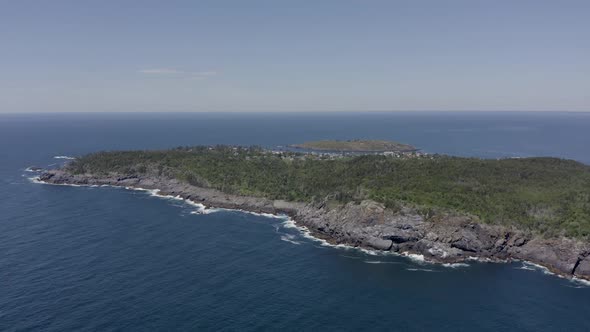 Drone flying high above a small island town with a rocky coastline in Maine