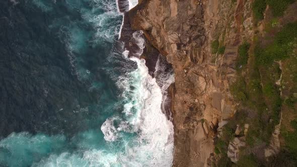 Ocean waves crashing and hitting against cliff and rocks bird eye view aerial drone shot.