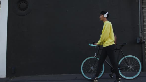 Transgender adult walking with a bike and using headphones