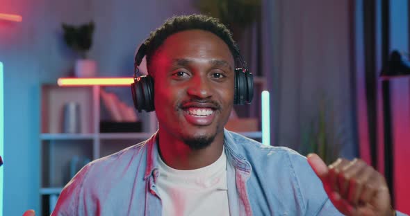 Guy in Headphones Making Dancing Movements while Listening Music in Colourful Lighted Room