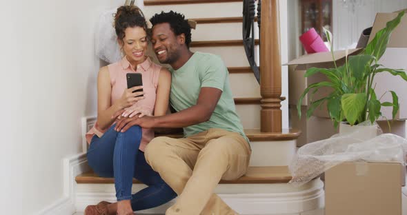 Happy biracial couple taking selfie on stairs of their new house