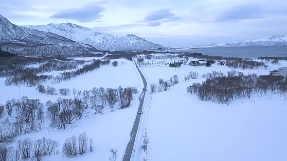 Aerial forward shot of car driving on road on Andoya Island during beautiful snowy winter day in Nor