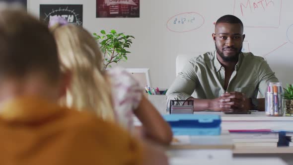 Video of happy african american male teacher sitting at desk during math lesson