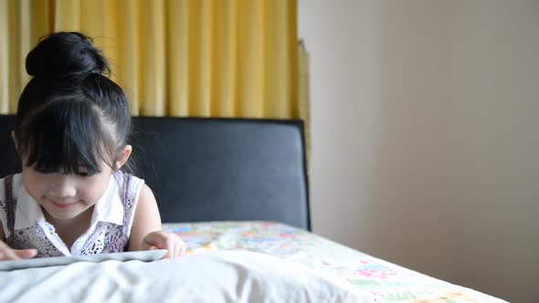 Little Asian Girl Using Tablet On Bed