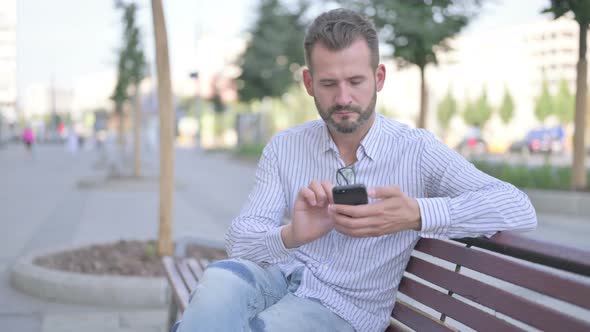 Young Adult Man Using Smartphone While Relaxing on Bench