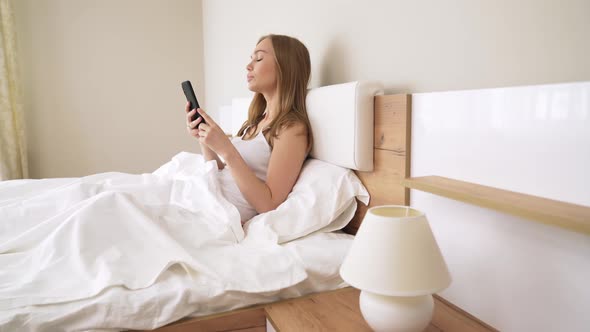 Young Woman Using Smartphone in Bed.