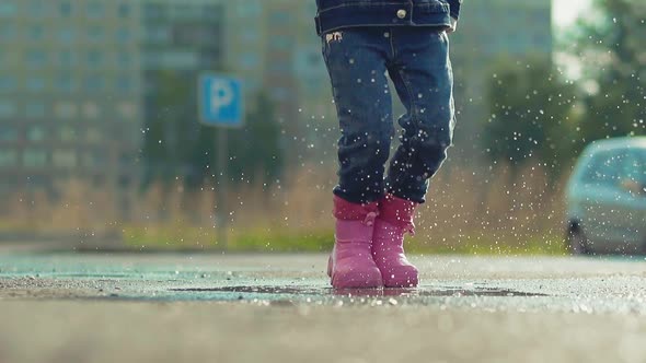 Funny Girl in Pink Rubber Boots Has Fun Jumping in Puddle