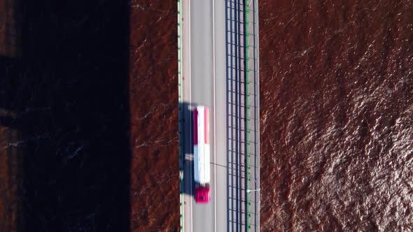 Concrete bridge over burgundy river due to impurities of snow in spring, cars drive across bridge