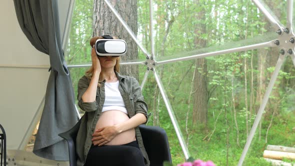 pregnant in virtual reality glasses stroking stomach overlooking the forest